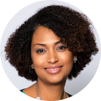 headshot of a dark-skinned woman with medium tightly-curly black hair, smiling at the camera, blue eyeshadow and a rope-like necklace.