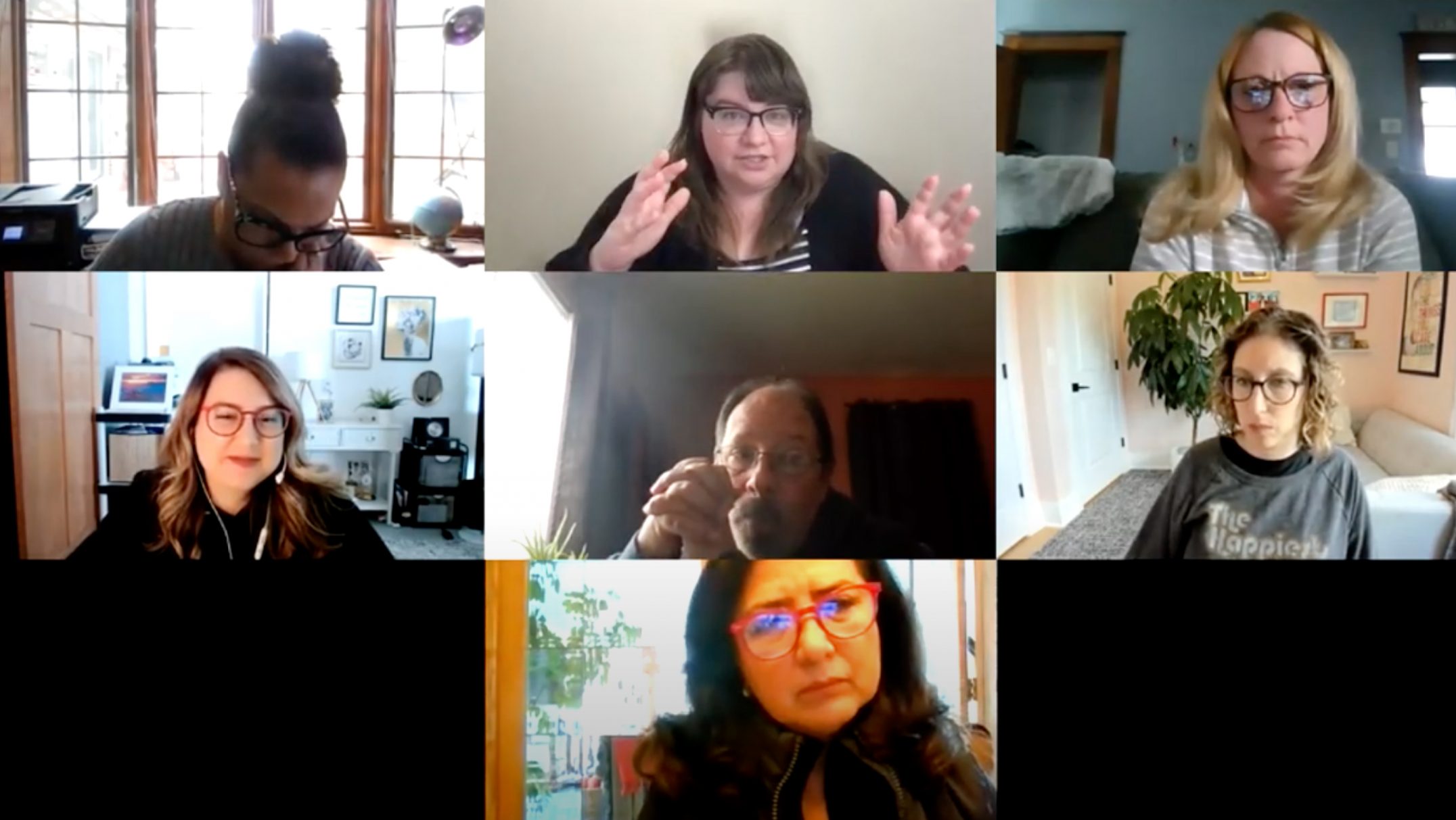 Zoom screen (video chat) grid of nine people with different backgrounds. The top row, center person is gesturing as though they are talking.