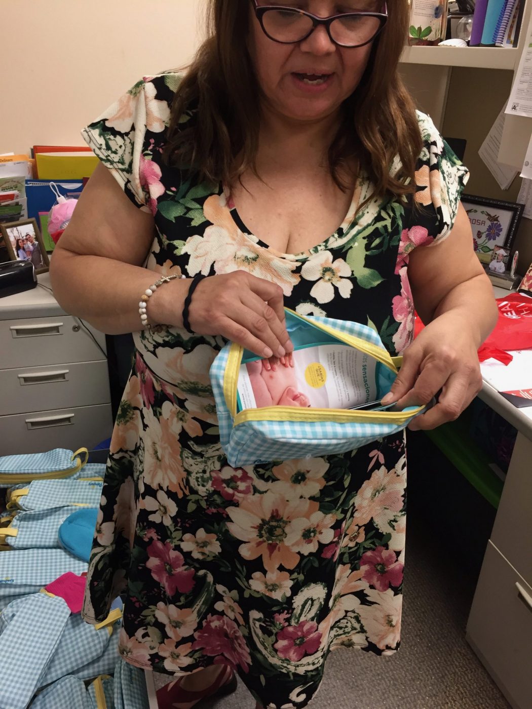 Woman in floral dress standing, holding open a small baby blue pouch with pamphlets inside